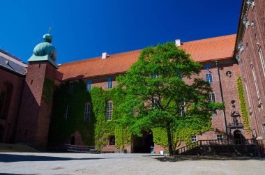 Avlu içinde Stockholm City Hall (Stadshuset) Nobel Ödülü ziyafet mahkemelerinin ve Belediye Meclisi bina Ivy ile kaplı tuğla duvarlar, döşenmiş çatı, kule, açık mavi gökyüzü, İsveç ile yeşil ağaç