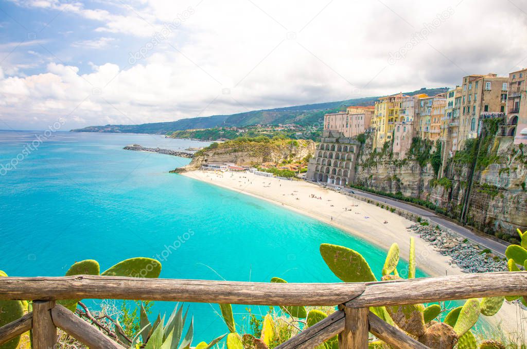 Tropea town and Tyrrhenian Sea beach, colorful buildings on top of high big rocks, view from Sanctuary church of Santa Maria dell Isola with fence foreground, Vibo Valentia, Calabria, Southern Italy