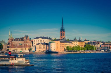 Riddarholmen Adası ilçe göl Malaren su Kungsholmen açık mavi gökyüzü ile Stockholm, İsveç demirlemiş tekne gemiyi Riddarholm kilise kulesi ve tipik İsveç renkli Gotik binalar,