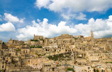 Sassi di Matera tarihi panoramik manzaralı Sasso Caveoso kaya mağara evlerin önünde mavi gökyüzü ve beyaz bulutlar, Unesco Dünya Mirası, Basilicata, Güney İtalya eski antik şehrin merkezi