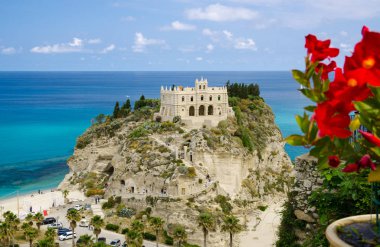 Manastır Sanctuary Santa Maria Kilisesi dell Isola üstünde tepe-in rock Tiren Denizi, mavi gökyüzü beyaz bulutlar açık yaz gün içinde ile bulanık kırmızı çiçekler ön plan, Tropea kasaba, Calabria, Güney İtalya