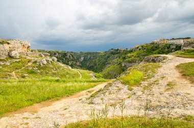 Nehri Vadisi uçurumu Kanyonu, kayalar, yeşil çimen, yol, mağaralar di ile görünümünü Murgia Timone ve koyu mavi gökyüzü arka plan yakınındaki eski antik kenti Matera (Sassi), Unesco miras, Basilicata, Güney İtalya