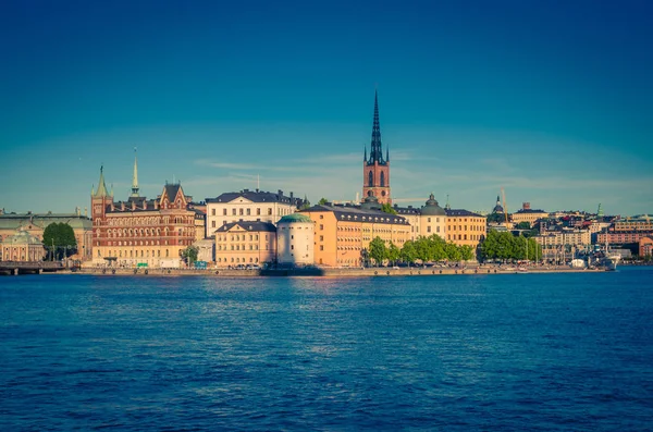 Riddarholmen 島地区リッダルホルム教会の尖塔と典型的なスウェーデンのカラフルなゴシック様式建物 青い澄んだ空 ストックホルム スウェーデンのクングスホルメンから湖メラーレン湖水に係留されたボート船 — ストック写真