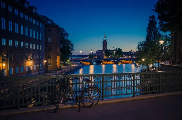 Bike, bicycle near bridge railing and Stockholm City Hall (Stadshuset) tower building, venue of Nobel Prize on Kungsholmen Island, Lake Malaren water at sunset, dusk, twilight, evening, Sweden