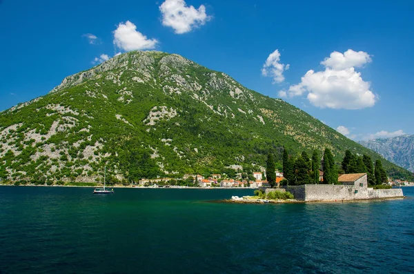 Saint George Benedictian monastery and church on St. George island Ostrvo Sveti Dorde in Boka Kotor bay near Perast town in front of mountains range and blue sky with white clouds, Montenegro