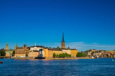 Riddarholmen Adası ilçe göl Malaren su Kungsholmen açık mavi gökyüzü ile Stockholm, İsveç demirlemiş tekne gemiyi Riddarholm kilise kulesi ve tipik İsveç renkli Gotik binalar,