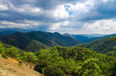 Kikkos Manastırı alan yeşil tepelerin ve çam ormanları önünde bulutlu gökyüzü, Kıbrıs Troodos Dağları aralığının panoramik üstten görünüm