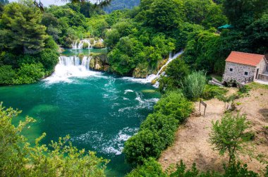 Yeşil bitkiler, ağaçlar, orman ve taş değirmen ile turuncu kiremit çatı Krka Milli Parkı'nda, Dalmaçya, Hırvatistan, Europe bina arasında güzel nehir şelaleler