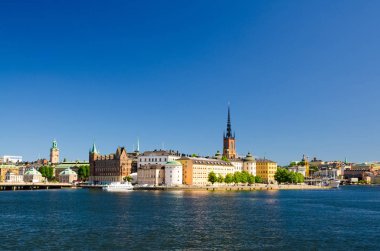 Riddarholmen Adası ilçe göl Malaren su Kungsholmen açık mavi gökyüzü ile Stockholm, İsveç demirlemiş tekne gemiyi Riddarholm kilise kulesi ve tipik İsveç renkli Gotik binalar,