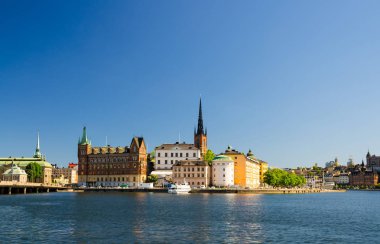 Riddarholmen Adası ilçe göl Malaren su Kungsholmen açık mavi gökyüzü ile Stockholm, İsveç demirlemiş tekne gemiyi Riddarholm kilise kulesi ve tipik İsveç renkli Gotik binalar,