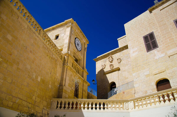 View of yellow buildings with watch in the old medieval Cittadella tower castle, also known as Citadel, Castello in the Victoria Rabat town, Gozo island, Malta