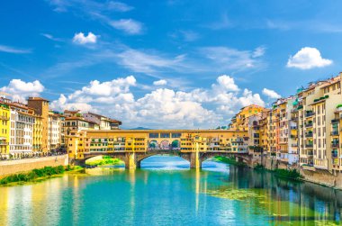 Floransa şehrinin tarihi merkezinde Arno Nehri mavi turkuaz su ve dolgu gezinti üzerinde renkli binalar evler ile Ponte Vecchio taş köprü, mavi gökyüzü beyaz bulutlar, Toskana, İtalya