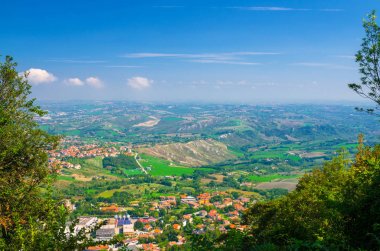 Vadi, yeşil tepeler, tarlalar ve mavi gökyüzü beyaz bulutlarıyla kaplı San Marino banliyö bölgesinin köylerinin panoramik manzarası. San Marino kalesinden görüntü