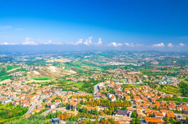 Vadi, yeşil tepeler, tarlalar ve mavi gökyüzü beyaz bulutlarıyla kaplı San Marino banliyö bölgesinin köylerinin panoramik manzarası. San Marino kalesinden görüntü