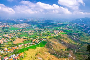 Vadi, yeşil tepeler, tarlalar ve mavi gökyüzü beyaz bulutlarıyla kaplı San Marino banliyö bölgesinin köylerinin panoramik manzarası. San Marino kalesinden görüntü