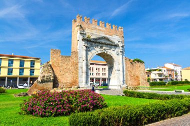 Augustus Arco di Augusto antik tuğla duvar ve taş kapı Arch kalıntıları, eski tarihi turistik şehir merkezi Rimini çiçek çalı ile yeşil çim, mavi gökyüzü arka plan, Emilia-Romagna, İtalya