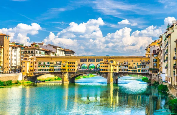 Floransa şehrinin tarihi merkezinde Arno Nehri mavi turkuaz su ve dolgu gezinti üzerinde renkli binalar evler ile Ponte Vecchio taş köprü, mavi gökyüzü beyaz bulutlar, Toskana, İtalya