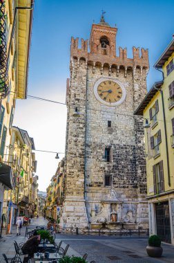 Brescia, İtalya, 11 Eylül 2019: Torre della Pallata tuğlalı ortaçağ saat kulesi binası tipik İtalyan caddesi, Brescia şehir tarihi merkezi, mavi gökyüzü, dikey manzara, Lombardy