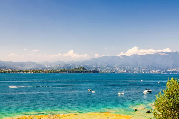 Jezioro Garda z łodziami motorowymi na błękitnej lazurowej turkusowej wodzie, wybrzeże z pasmem górskim — Zdjęcie stockowe