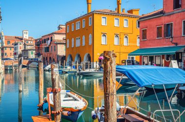 Dar su kanalı Vena ile Chioggia şehri eski renkli binalar ve tuğla köprü arasında demirlemiş tekneler ile yaz günü mavi gökyüzü arka planı, Veneto Bölgesi, Kuzey İtalya