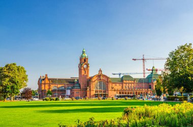 Wiesbaden Hauptbahnhof merkez tren istasyonu Neo-barok tarzı bina ve Reisinger-Anlagen parkı tarihi şehir merkezinde yeşil ağaçlar ve çimenler, mavi gökyüzü arka planı, Hesse eyaleti, Almanya
