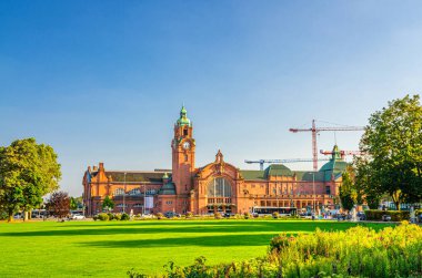 Wiesbaden Hauptbahnhof central railway station Neo-baroque style building and Reisinger-Anlagen park with green trees and lawn in historical city centre, blue sky background, State of Hesse, Germany clipart