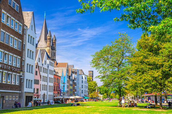 Cologne, Germany, August 23, 2019: typical german houses and buildings and green grass lawn with trees near promenade of Rhine river in historical city centre, people tourists having a rest