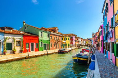 Burano adasının renkli evleri. Balıkçı tekneleri ve ahşap köprüsü olan dar su kanalının fondamenta dolgusu üzerinde çok renkli binalar, Venedik Bölgesi, Kuzey İtalya