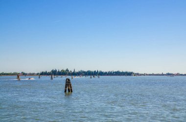 Venedik lagün suyundaki San Francesco del Deserto adasının ahşap direklerle panoramik manzarası. Burano adasının manzarası. Venedik Eyaleti, Veneto Bölgesi, Kuzey İtalya