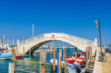 Taş köprü Ponte di Vigo Vena su kanalı boyunca, Chioggia şehrinin tarihi merkezinde iskele kenarında renkli tekneler, yaz günü mavi gökyüzü arka planı, Veneto Bölgesi, Kuzey İtalya