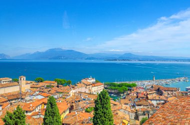 Desenzano del Garda kasabasının hava panoramik manzarası, kırmızı kiremitli çatı binaları, Garda Gölü su yüzeyi, Monte Baldo dağ sırası, Sirmione yarımadası, molo iskelesi deniz feneri, Lombardy, Kuzey İtalya