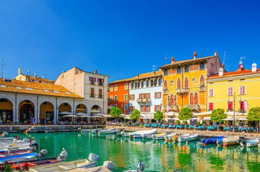 Desenzano del Garda, İtalya, 11 Eylül 2019: Turkuaz sudaki eski liman Porto Vecchio, yeşil ağaçlar, sokak restoranları ve tarihi şehir merkezinde geleneksel binalar, Lombardy