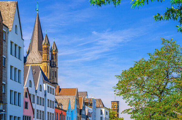 Row of colorful facade buildings, Great Saint Martin Roman Catholic Church tower with spire and green trees in historical city centre, blue sky in sunny summer day, North Rhine-Westphalia, Germany