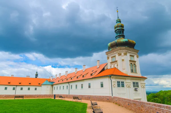 Jesuit College building, green grass lawn and benches in Park GASK, Kutna Hora historical Town Centre, blue dramatic sky background, Central Bohemian Region, Czech Republic