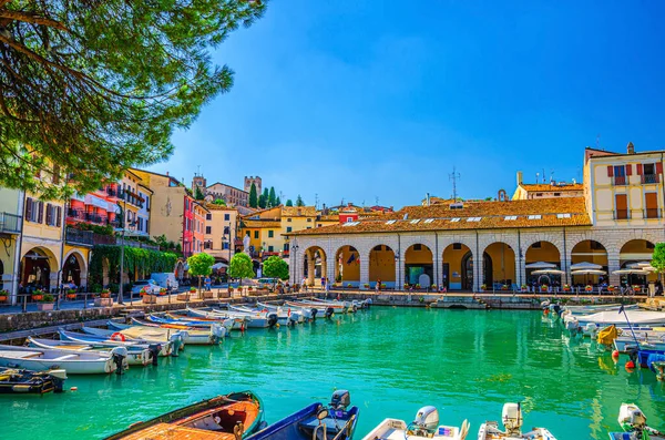 Eski liman Porto Vecchio motorlu tekneleri turkuaz sularda, yeşil ağaçlar ve geleneksel binalar Desenzano del Garda 'nın tarihi merkezinde, mavi gökyüzü arka planı, Lombardy, Kuzey İtalya