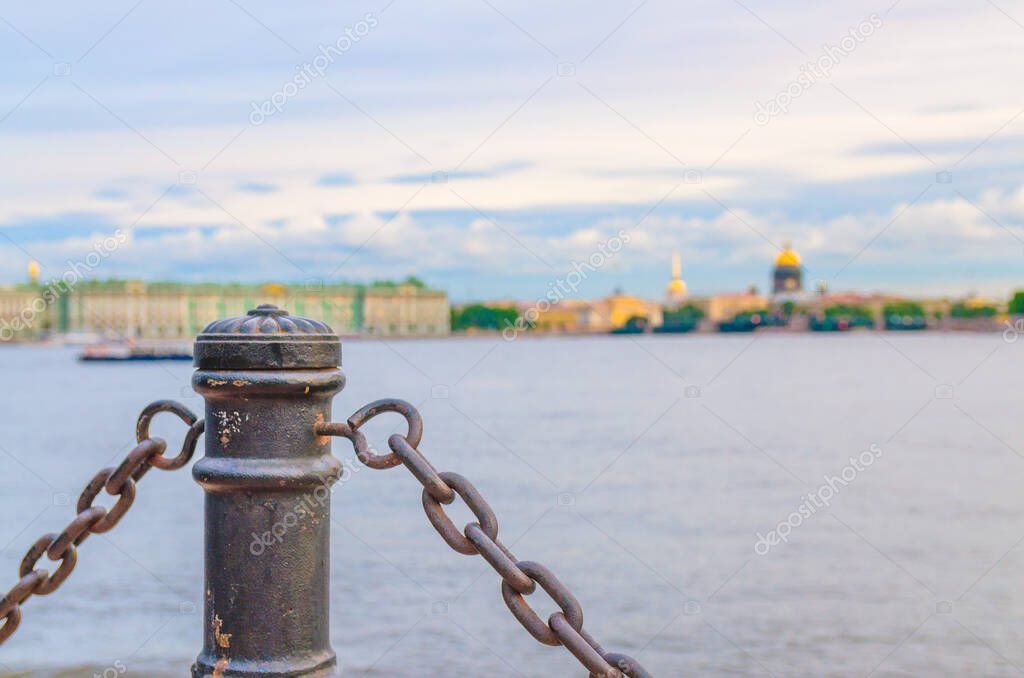 Fencing chain post with blurred background of Neva river, cityscape of Saint Petersburg Leningrad city with Winter Palace, State Hermitage Museum, Saint Isaac's Cathedral, Russia