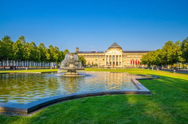 Wiesbaden, Almanya, 24 Ağustos 2019: Kurhaus or cure house spa and casino building and Bowling Green park with grass lawn, trees alley and lake with Fountain in history city center, State of Hesse