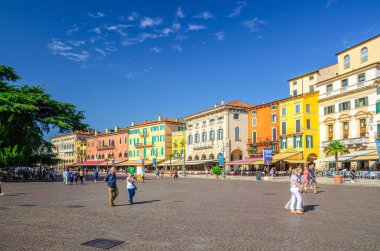 Verona, İtalya, 12 Eylül 2019: Tarihsel şehir merkezinde eski renkli binalar, kafeler ve restoranlar, yeşil ağaçlar ve yürüyen turistler, mavi gökyüzü