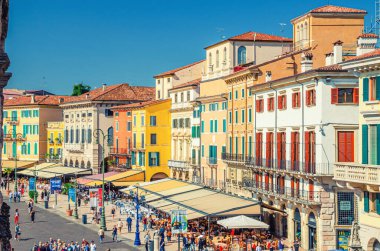 Verona, İtalya, 12 Eylül 2019: Tarihi kent merkezinde Piazza Sütyen Meydanı 'ndaki eski renkli binalar, çadırları ve yürüyen turistleri olan kafeler ve restoranlar, hava manzaralı