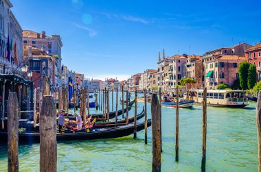 Venedik, İtalya, 13 Eylül 2019: Gondolcu, Grand Canal su yolu üzerindeki geleneksel gondolcu, ahşap iskele rıhtımı, tipik renkli binalar ve yelkenli tekne arka planı.