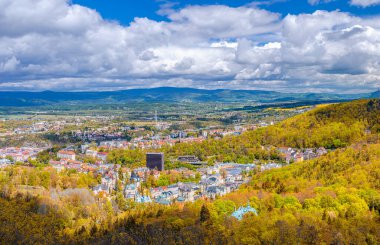 Karlovy Vary şehrinin havadan panoramik manzarası. Tarihi şehir merkezinde renkli binalar ve spa otelleri var. Sonbaharda Karlsbad kasabasının ve Ore dağlarının manzarası