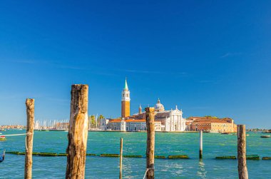 San Giorgio Maggiore adası Campanile San Giorgio ile Venedik Gölünde, San Marco havzasının su kıyısında ahşap kutuplar, açık mavi gökyüzü, Veneto Bölgesi, İtalya, Venedik şehir manzarası