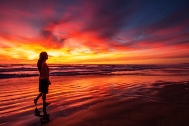 gün batımında sahilde tek başına yürüyen kadın