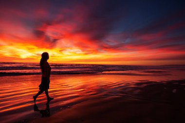 gün batımında sahilde tek başına yürüyen kadın