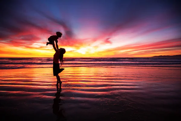 Anya és fia szórakozik naplementekor a strandon — Stock Fotó