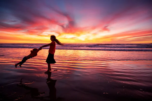 Madre e figlio si divertono al tramonto sulla spiaggia — Foto Stock