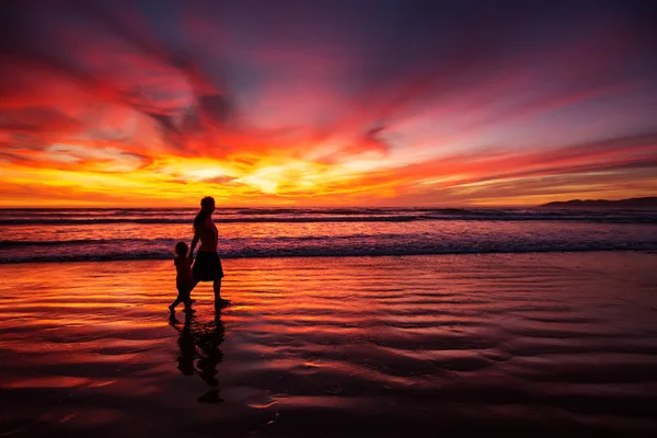 Mãe e filho se divertindo ao pôr do sol na praia — Fotografia de Stock