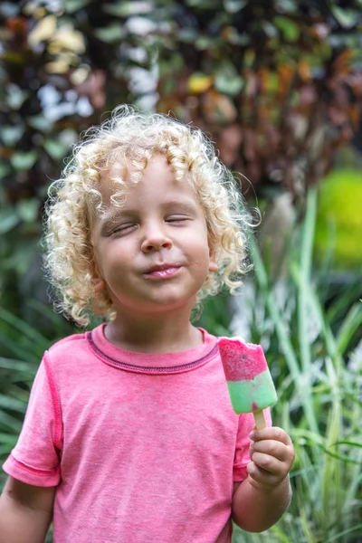 Malý chlapec s blond kudrnatými vlasy žere zmrzlinu — Stock fotografie