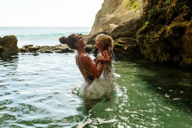 Anne ve çocuğu okyanusun kenarında doğal bir havuzda.