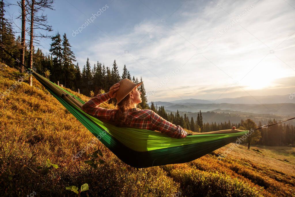 Woman hiker resting after climbing in a hammock at sunset